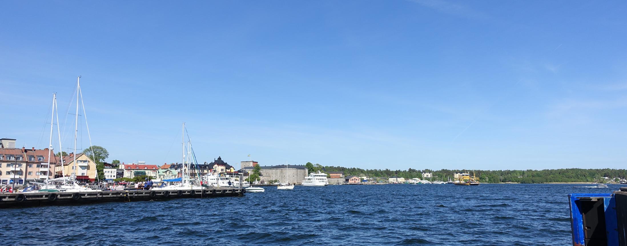 sommarquiz frågor om platser och personer i Sverige. Bilden med hav och båtar visar Vaxholms hamn och längre bort Vaxholms fästning